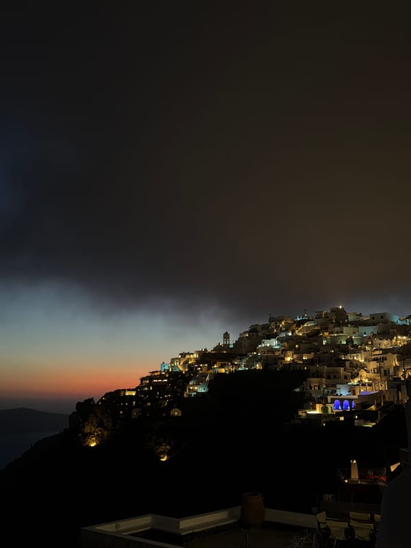 Evening lights illuminate cliffside buildings in Thira, Greece