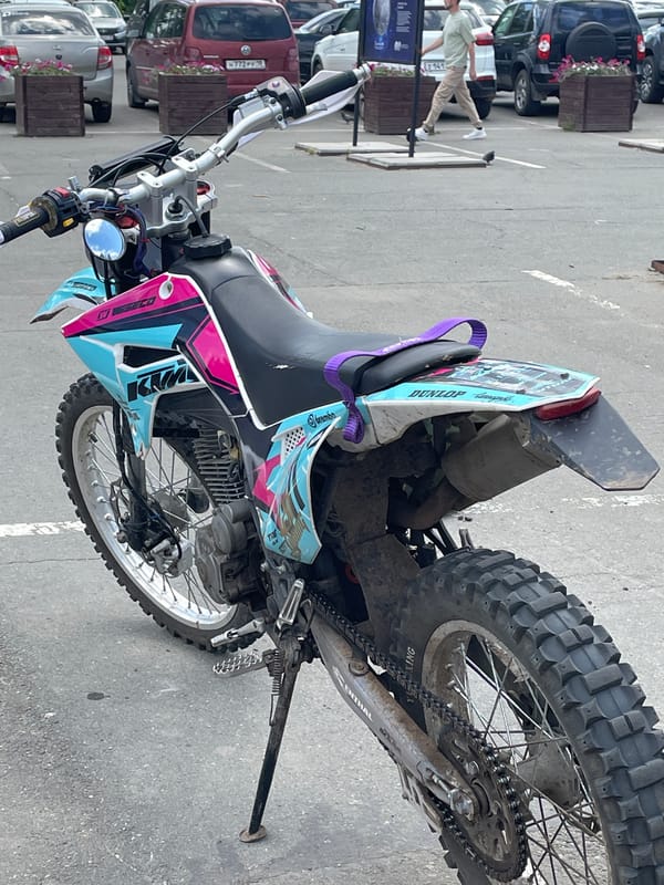Urban scene captures parked dirt bike, white statues against blue sky