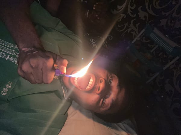 Lighter flame held to face in dim Ihiagwa home