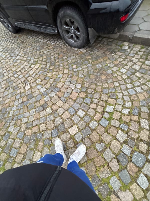 Person stands beside black car on cobblestone street in Sopot