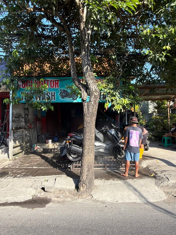 Roadside motorcycle wash spot under a shady tree, North Kuta
