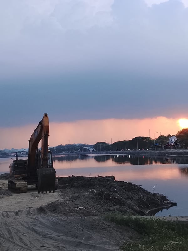 Excavators at the Lhokseumawe waterfront during a vivid sunset