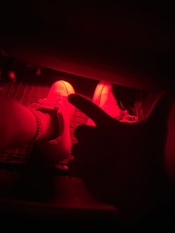 Person in white sneakers captured in red-lit vehicle interior