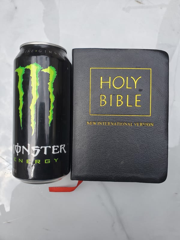 Monster Energy can photographed beside Bible on marble surface