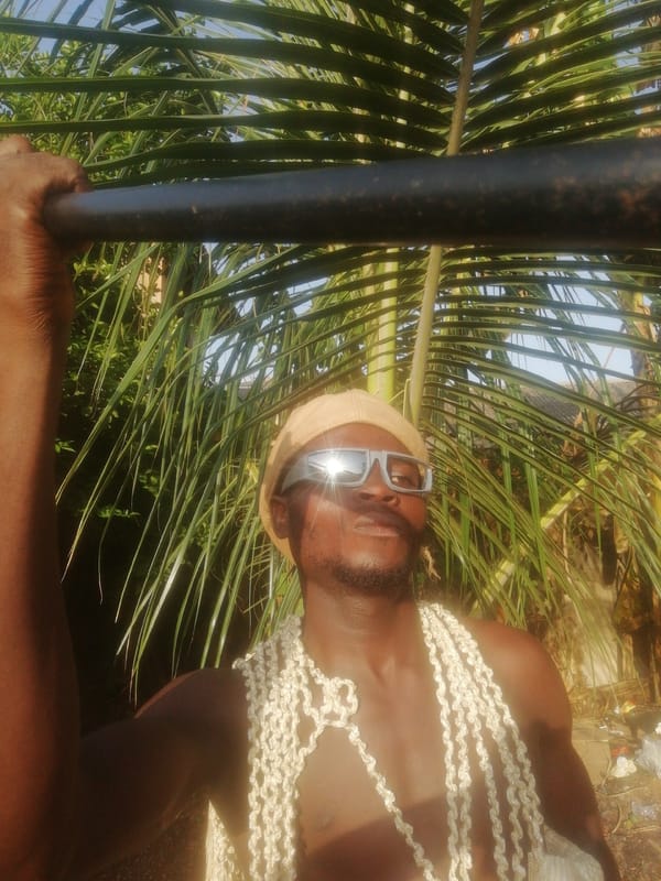 Men in tropical setting, one feeding chickens, another in shell garlands