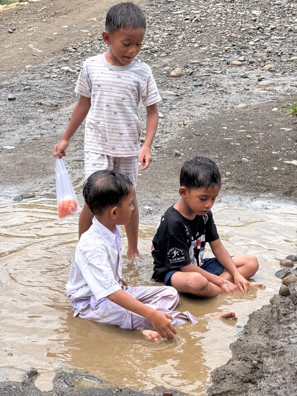 Kids in school uniforms splash through muddy puddles in rural Indonesia