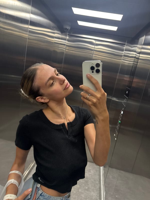Woman with medical wristband takes elevator selfie, drinks vitamin water