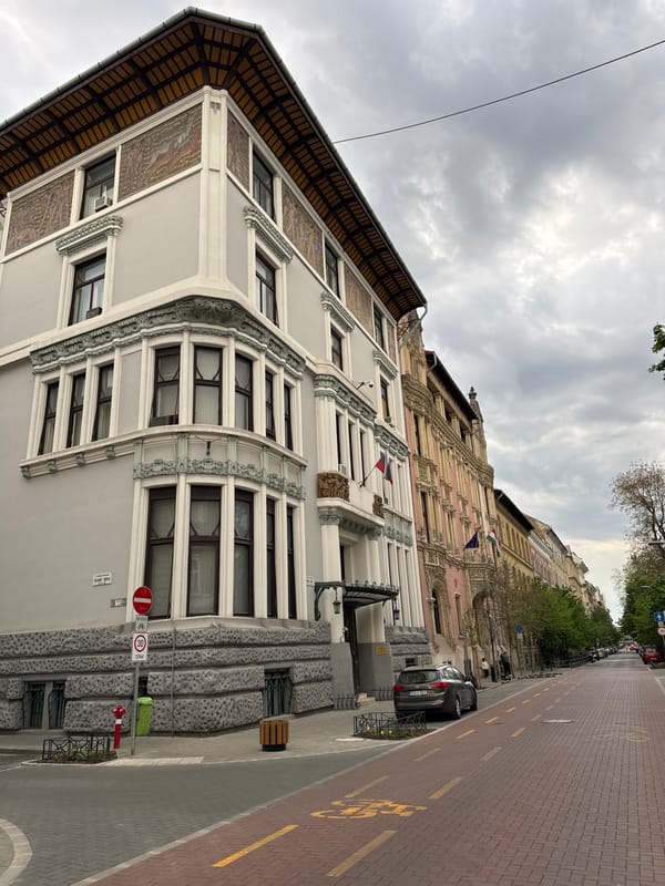 Motorcyclist pauses on ornate Budapest street near white car