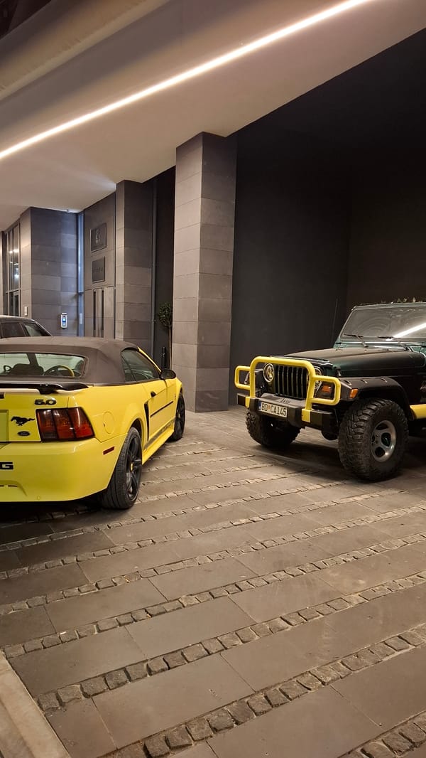 Yellow Mustang, dark Jeep parked on stone paving in Budva