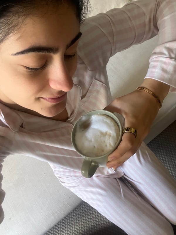 Woman enjoys breakfast in bed with latte and yogurt bowl