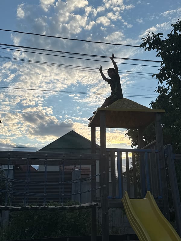 Arms raised atop a playground structure against a Chișinău sunset