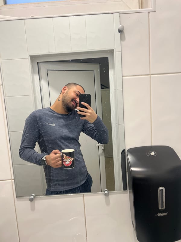 Man takes bathroom mirror selfie with phone and mug