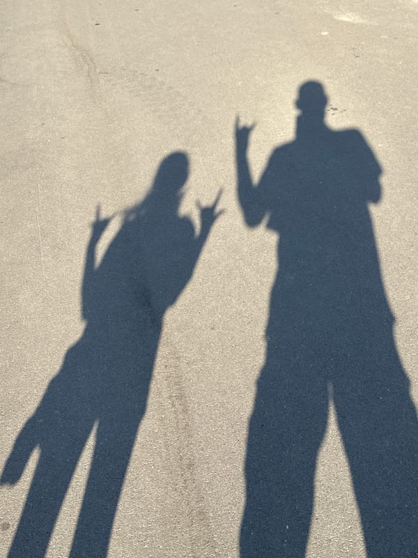 Peace sign shadow and a larger silhouette on asphalt