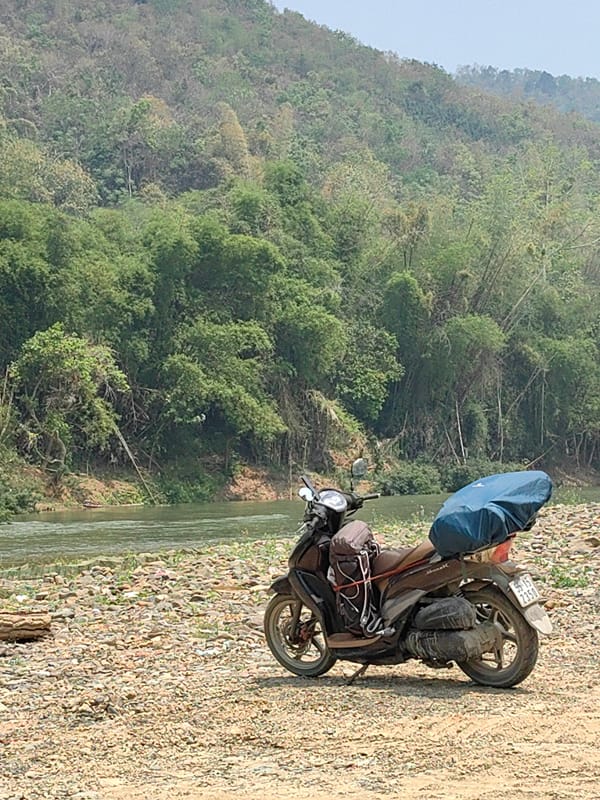 Loaded scooter parked on rocky rivershore in Vietnam