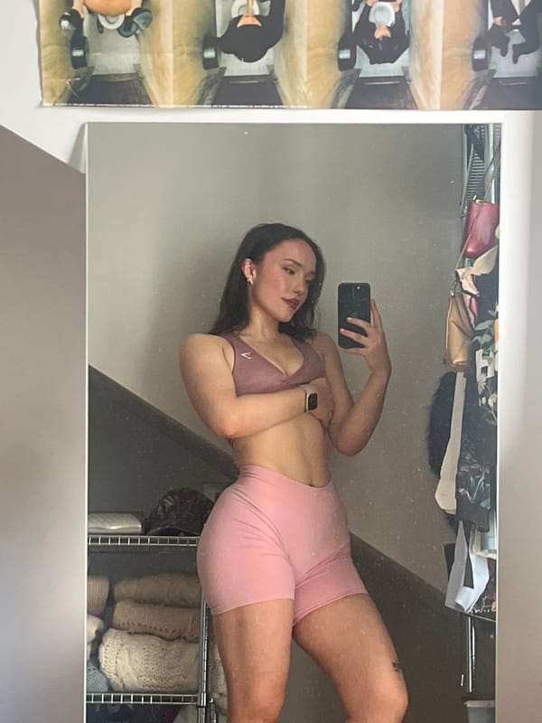 Woman takes mirror selfie in pink sportswear, London closet