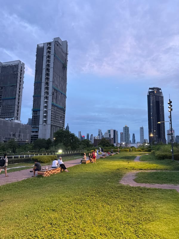 Lumphini Park at dusk, city skyline looming behind the green
