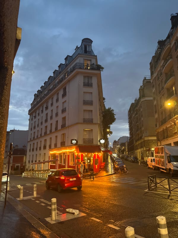 Wet Paris streets glow at dusk near a red storefront