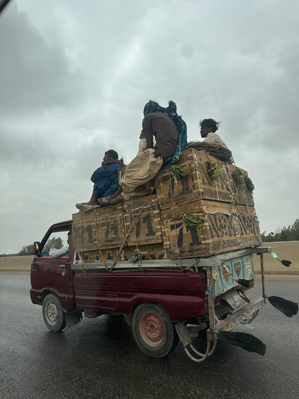 Crate-loaded pickup truck navigates wet Karachi roads in overcast conditions