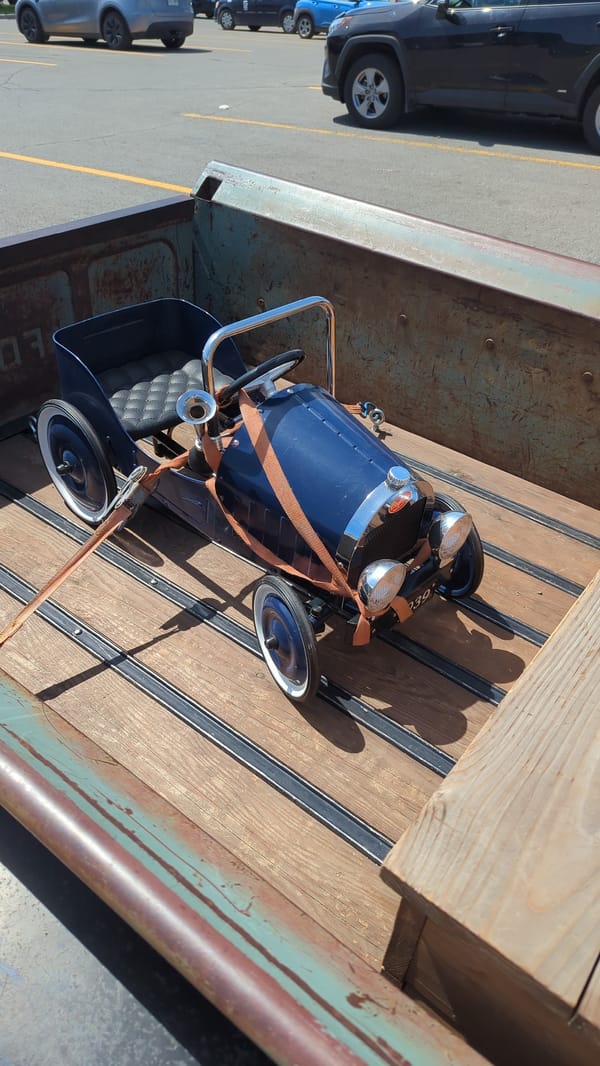 Rusty 1951 Ford F-1 hauling a Bugatti pedal car in Laval