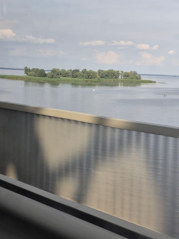 Driving past a calm river or lake, islands in view