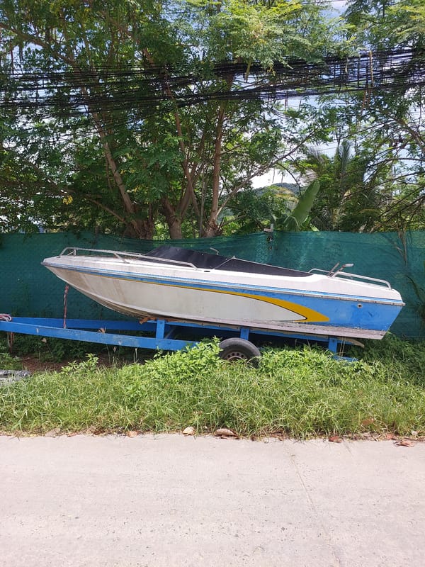 Older motorboat on trailer parked roadside in Baan Tai
