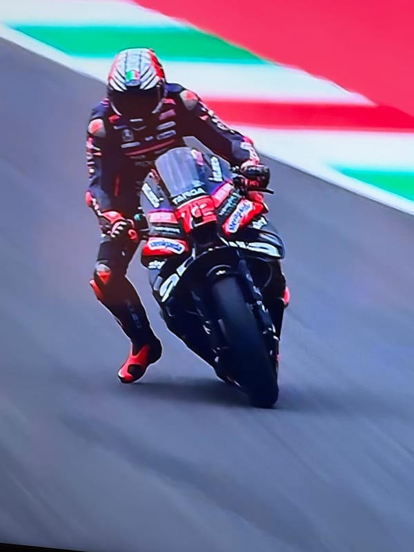 Motorcyclist leans into turn on track with Italian flag backdrop