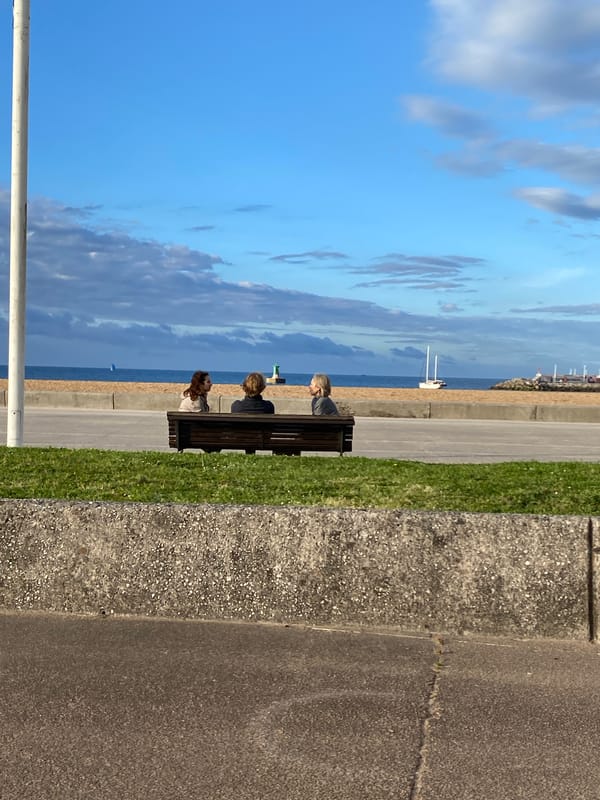 Three people rest on bench at Gijón seafront promenade