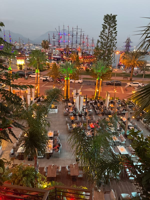 Alanya harbor lights up at dusk with pirate ships and waterfront dining