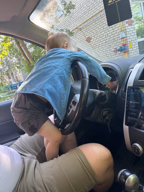 Toddler plays with steering wheel on adult's lap in Russia