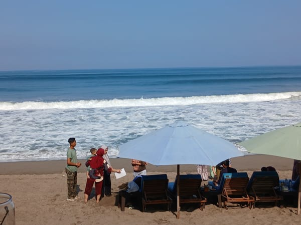 Dark sand beach in Bali with statue, chairs, and shoreline
