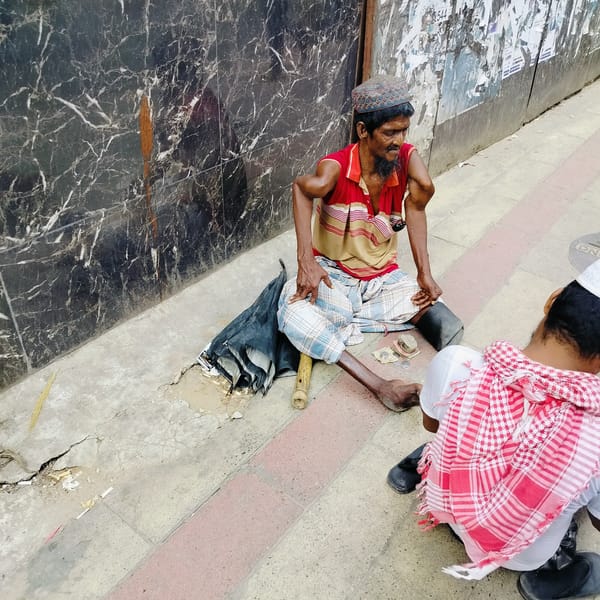 Two men sit on sidewalk in Dhaka street scene