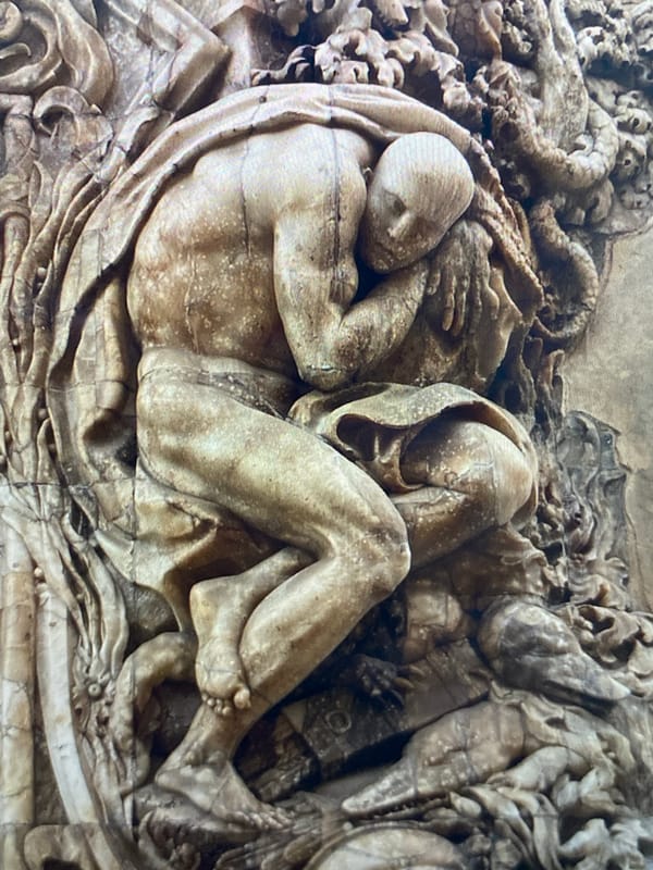 Relief carving of a curled, distressed figure in close detail