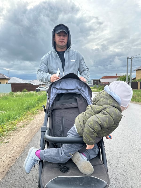 Father pushes stroller through wet streets in Éstachi, Russia