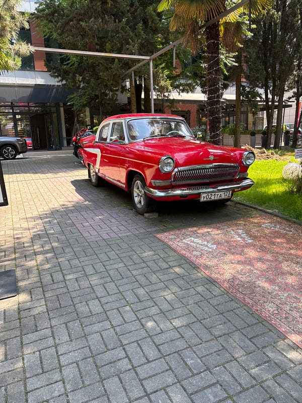 Sochi street life centers on a parked vintage Volga and busy sidewalks.