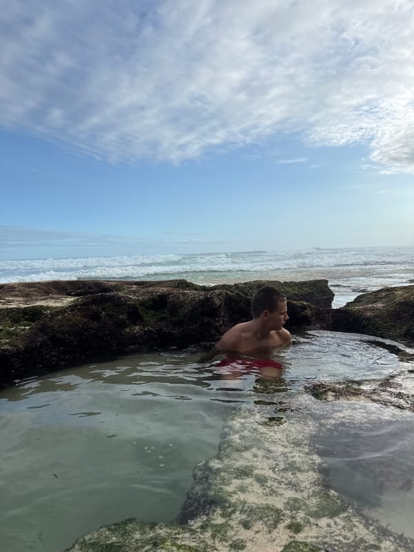 Man explores tide pools at rocky beach in Kuta Selatan