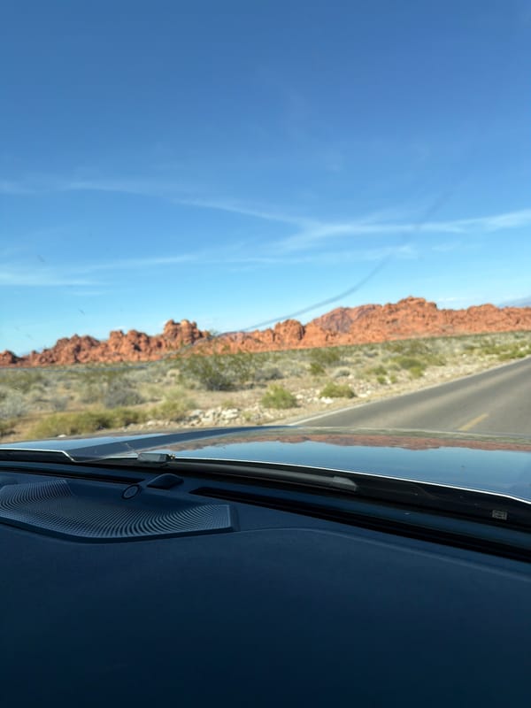 Driver captures desert landscape with red rocks through windshield