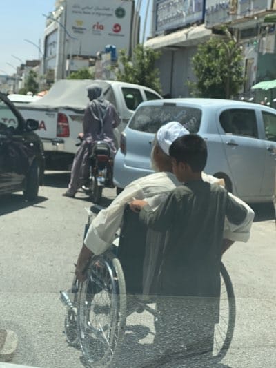Boy helps elderly man in wheelchair on Kandahar street