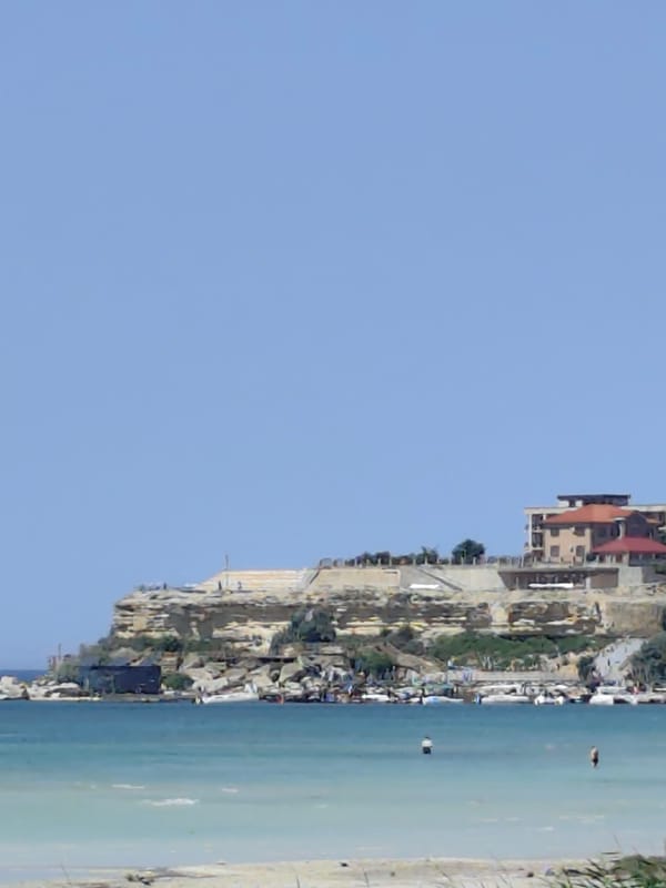 Aktau's Caspian cliffside — buildings, reeds, and calm water