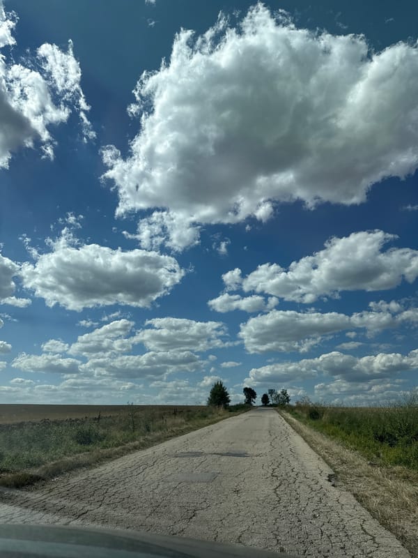 Cracked rural road cuts through dry Bulgarian countryside under summer skies