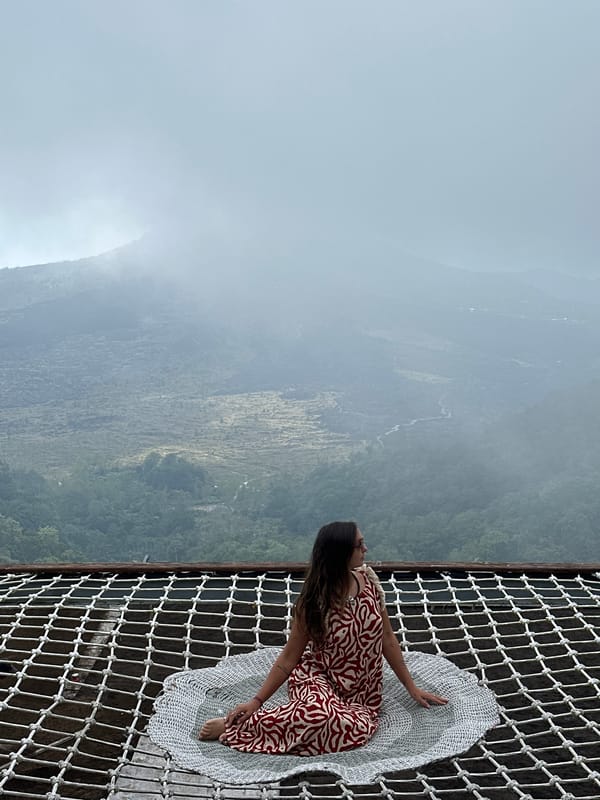 Woman sits on suspended net overlooking Kintamani mountains