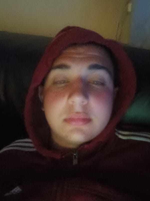 Person in Adidas hoodie rests on couch while using phone