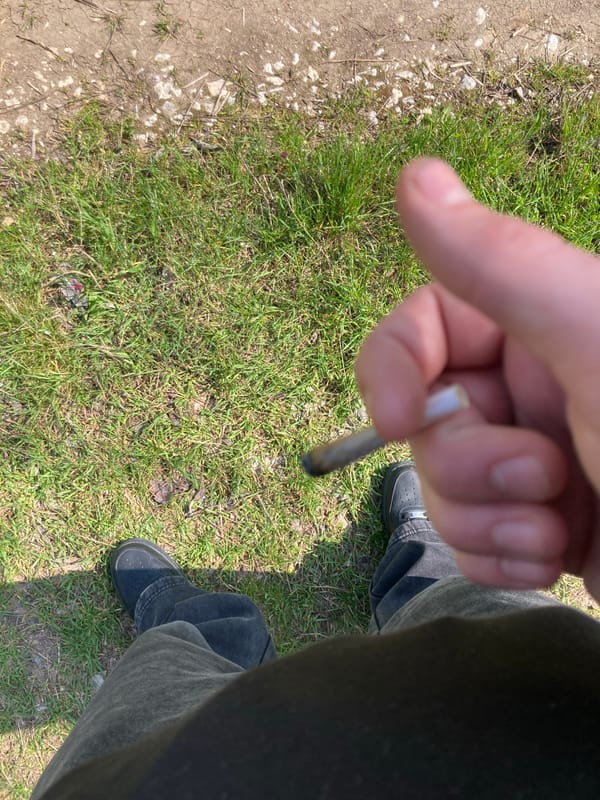 Person smoking cigarette on grass near dirt path