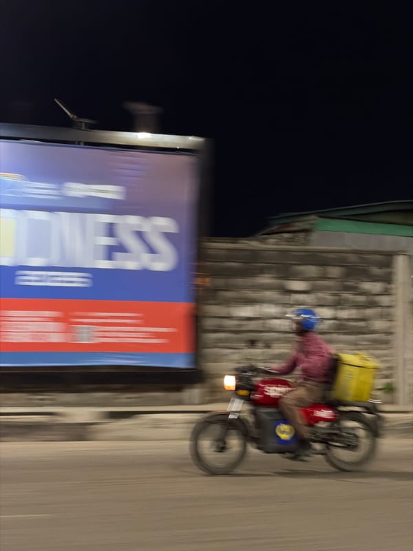 Delivery rider passes billboard on Itirin street at night