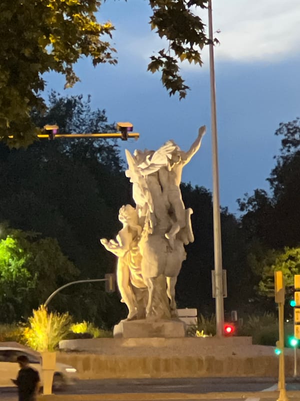Evening streetlights illuminate three-figure stone sculpture in Madrid