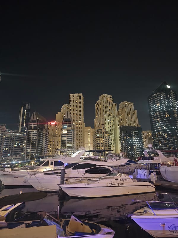 Dubai Marina at night, boats docked, skyline glowing