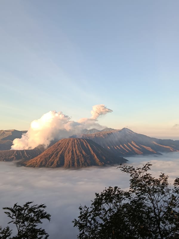 Mount Bromo erupting at sunrise, crowds gathering at viewpoints