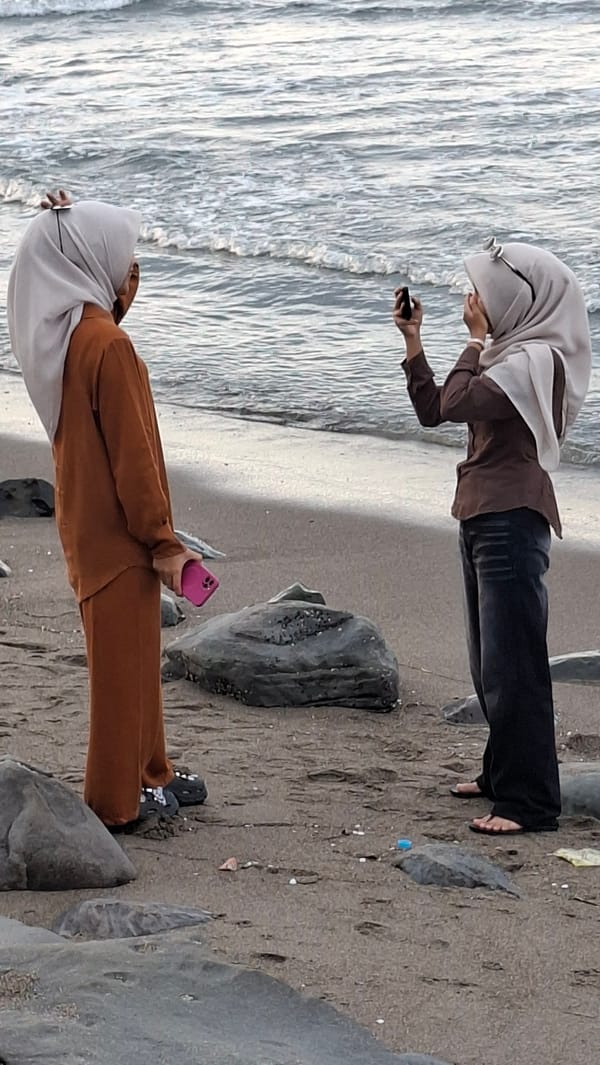 Lhokseumawe beach afternoon: surfers, shoreline hangouts, passing cargo ship