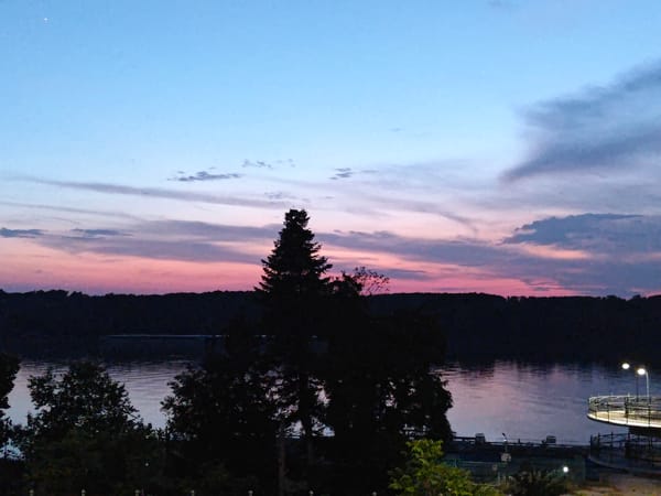 Dusk falls over a waterfront street, sky shifting to purple and pink