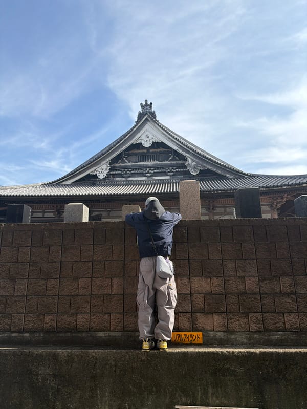 Person rests against wall near traditional building in Taito