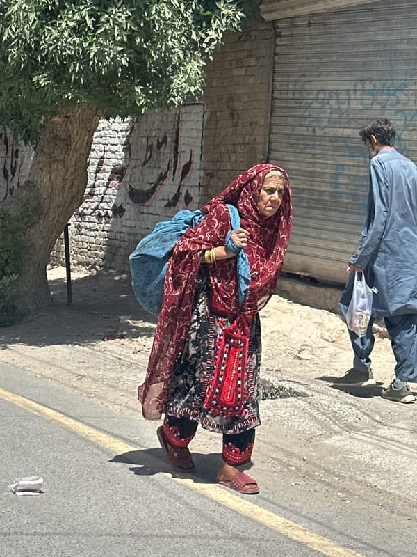 Elderly woman in traditional dress walks Quetta street